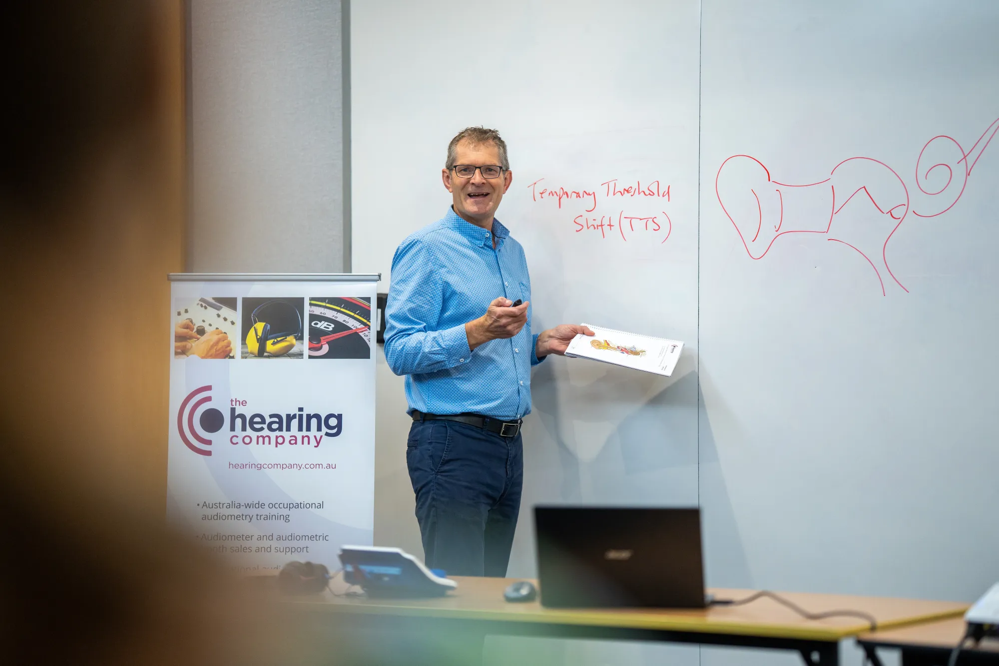 Director Glenn Johnson smiling and looking at the camera while teaching in front of a whiteboard.
