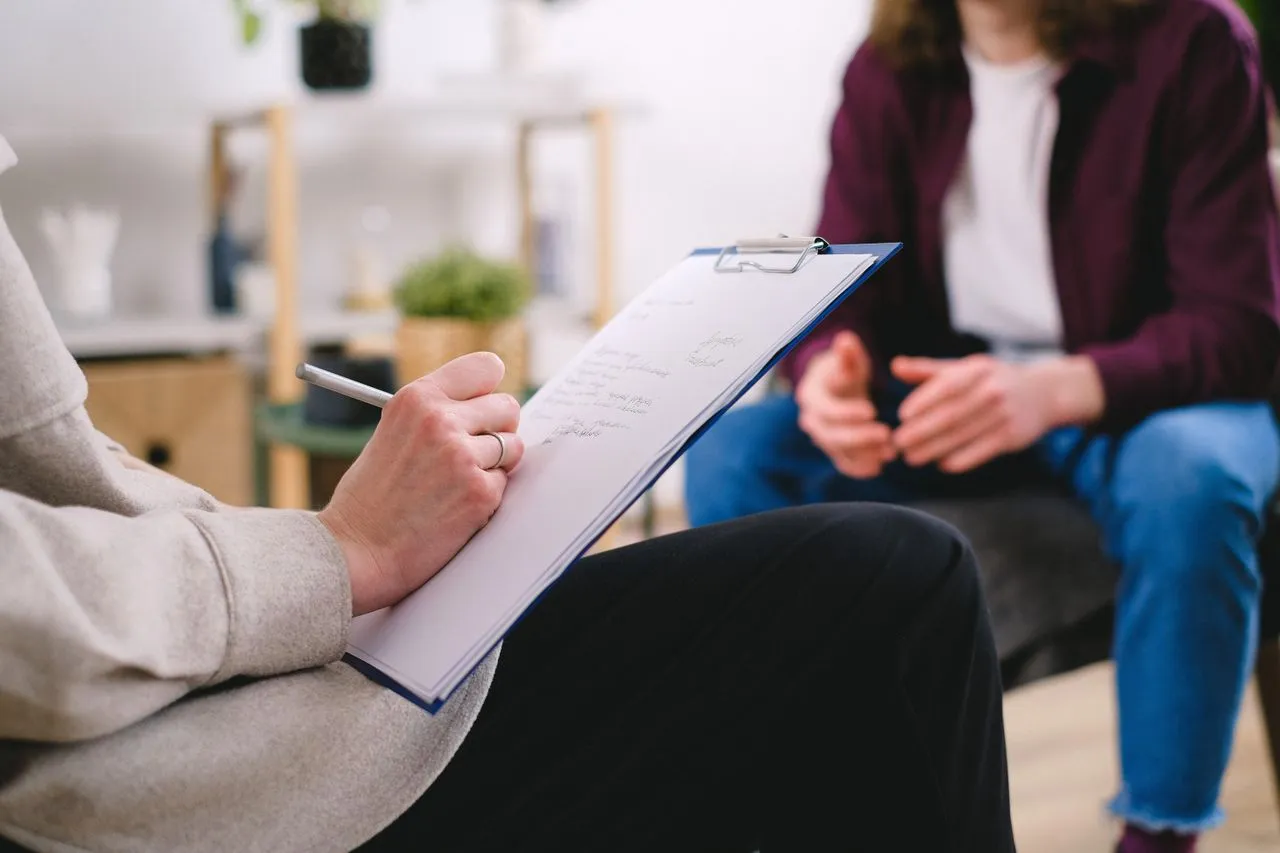 Healthcare worker evaluating a patient while writing on a clipboard.